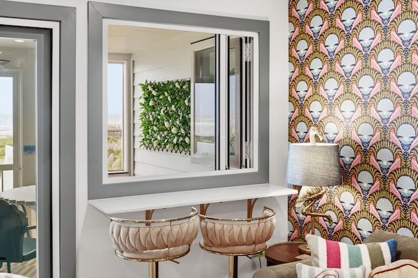Un interior moderno con una consola blanca, dos sillones tapizados, un papel tapiz estampado y vistas al exterior a través de una ventana.
