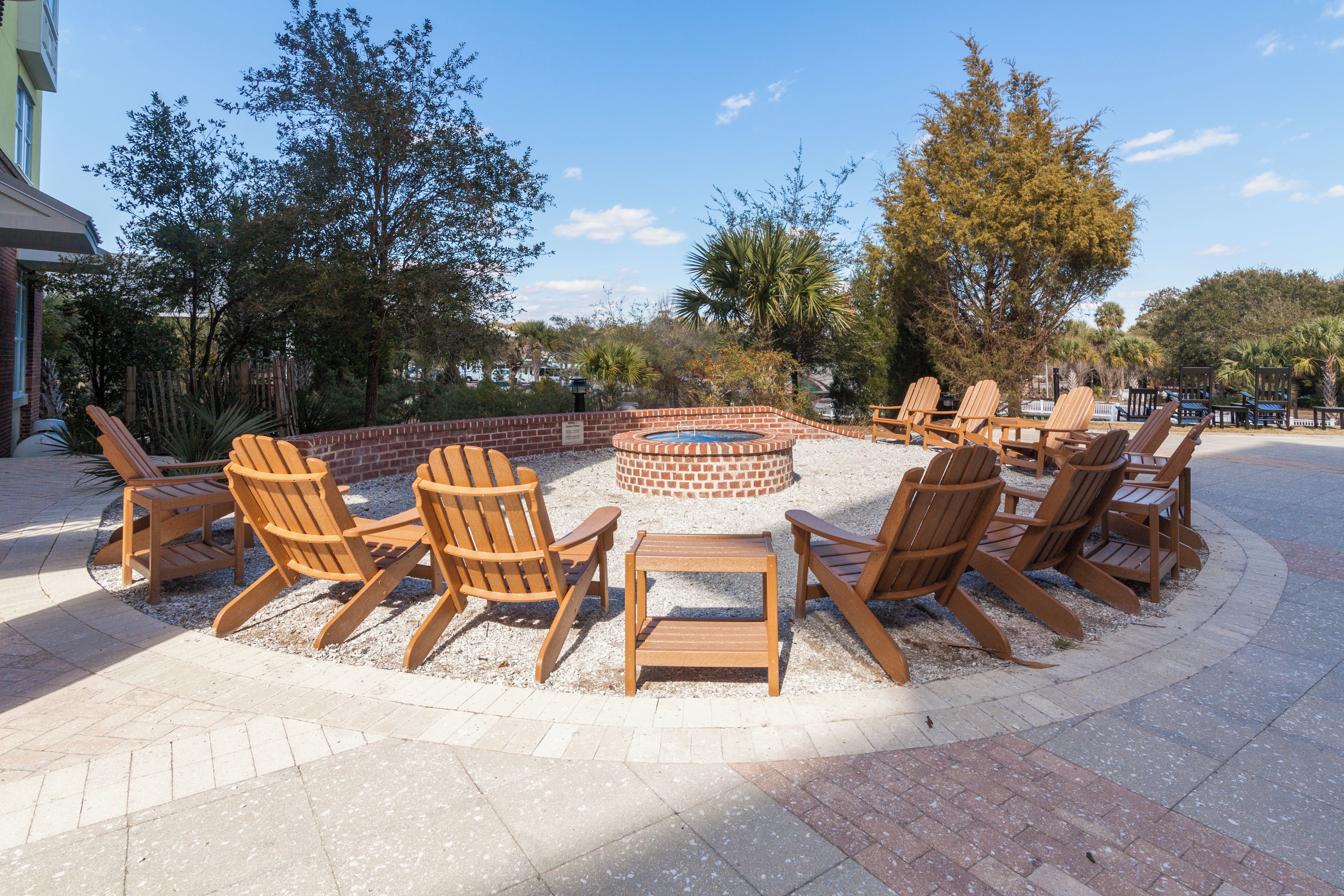 A circular seating area with Adirondack chairs around a central fire pit, surrounded by a brick wall and gravel ground.