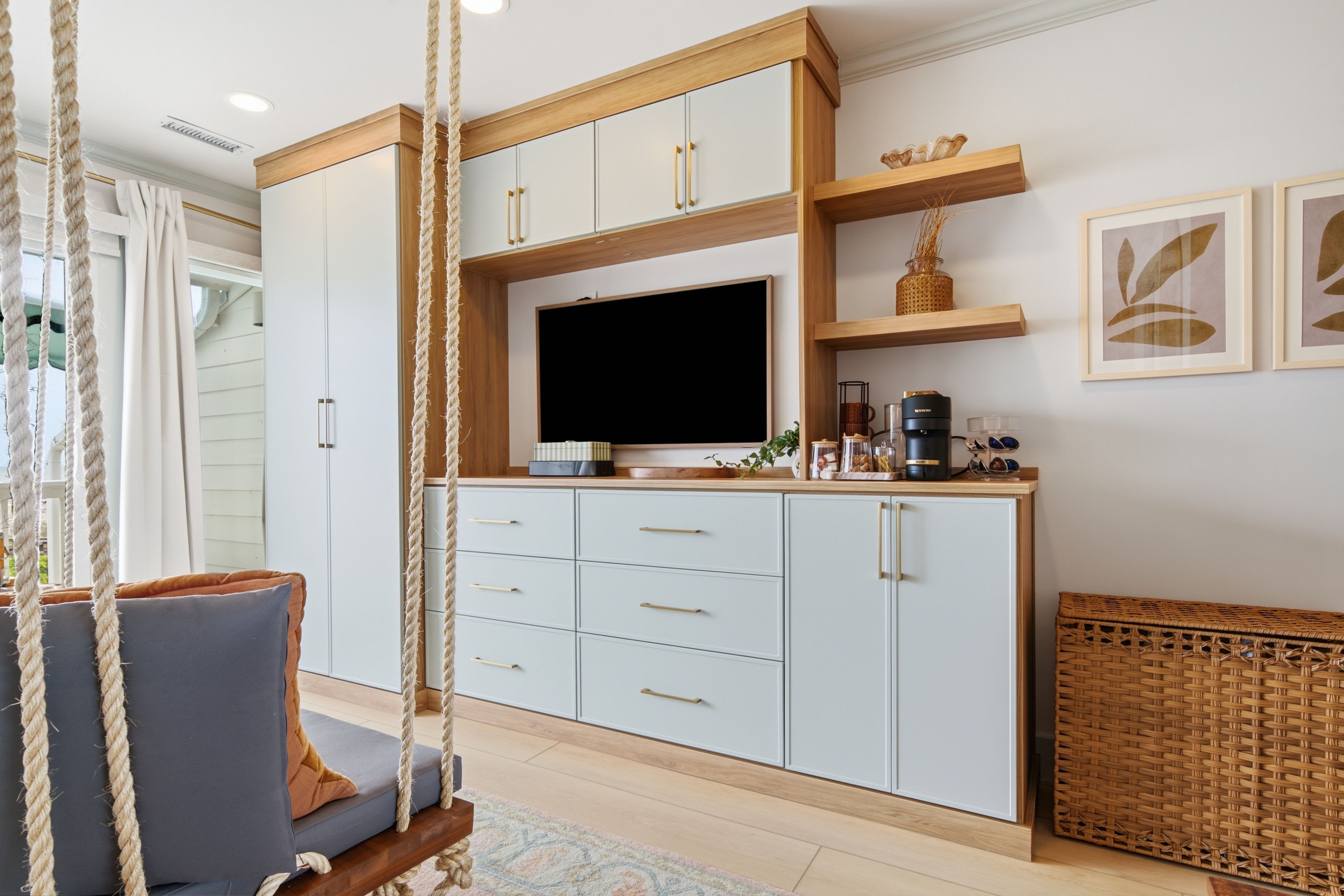 A modern living room with a swing chair, a flat-screen TV, and a kitchen area with cabinets and a coffee machine.