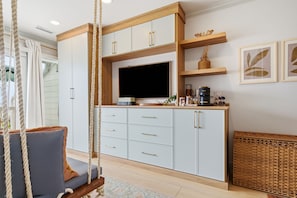 Una sala moderna con un sillón colgante, un televisor de pantalla plana y una zona de cocina con armarios y una cafetera.