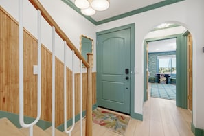 Un pasillo con una escalera de madera, una puerta verde y vista a una habitación con alfombra estampada.