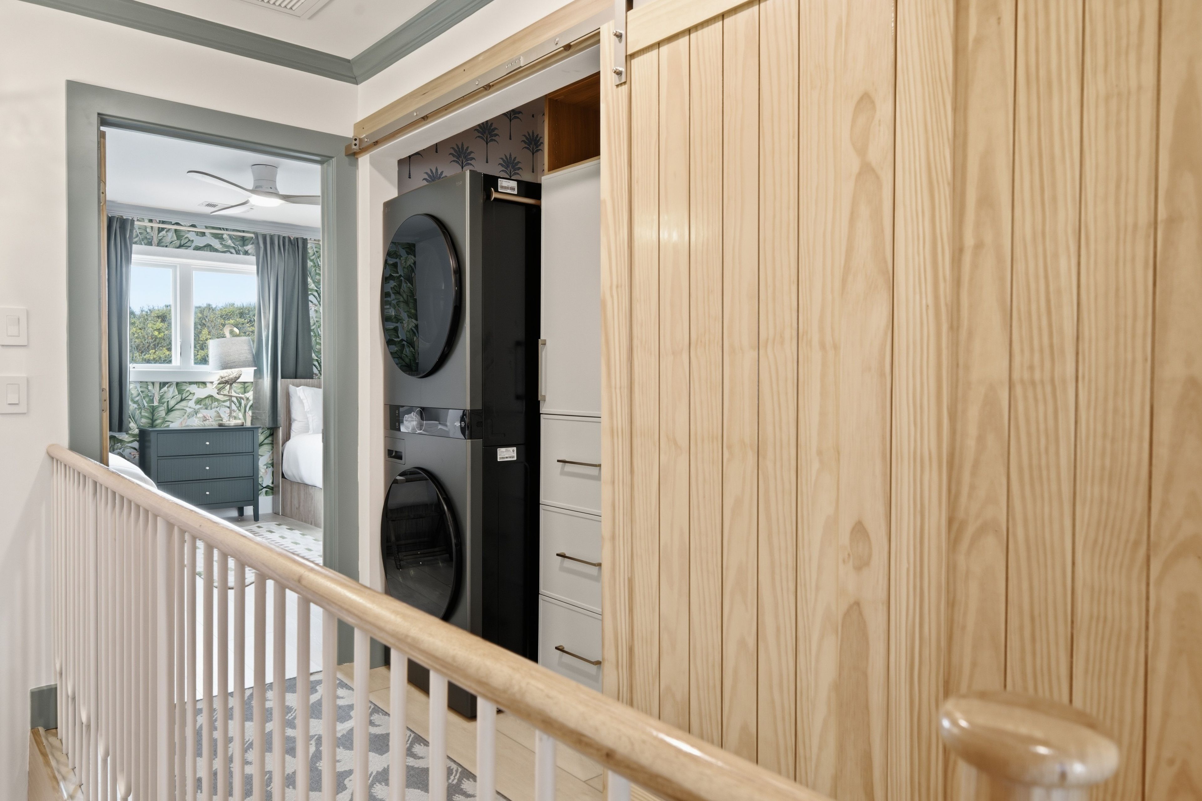 A staircase with a wooden handrail leading to a room with a washing machine and a small table.