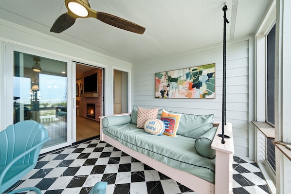 A room with a checkered floor, a light blue sofa with pillows, a ceiling fan, and a painting on the wall.