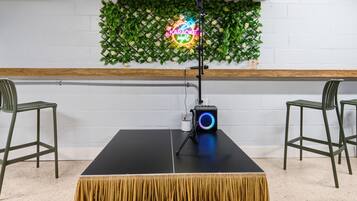 A room with a black table, two chairs, a neon sign, and a wall decorated with green foliage.