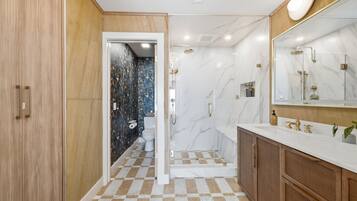 A bathroom with a checkered floor, a shower, a toilet, and a vanity with a mirror.