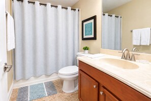A bathroom with a shower curtain, toilet, sink, mirror, and a framed quote on the wall. - 6BR Family Vacation Home Paradise Palms Private Pool Near Disney (Kissimmee)