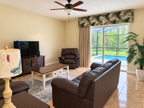 A living room with a sofa, armchair, TV, and a ceiling fan. - 6BR Family Vacation Home Paradise Palms Private Pool Near Disney (Kissimmee)