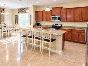 A kitchen with wooden cabinets, a microwave, a stove, and a dining area with chairs and a table. - 6BR Family Vacation Home Paradise Palms Private Pool Near Disney (Kissimmee)