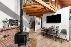 A cozy living room with a brick fireplace, a dining area with a table and chairs, and a staircase leading to an upper level. - Petros Place Ptarmigan Village Hot Tub Pool (Whitefish)
