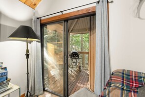 A room with a sliding glass door leading to an outdoor deck, a lamp, and a plaid blanket on a chair. - Petros Place Ptarmigan Village Hot Tub Pool (Whitefish)