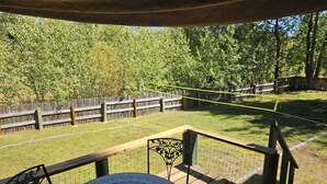 A wooden deck with a round table and chairs, a fenced yard, and a wooden fence in the background.