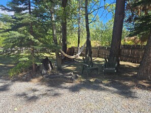 A forested area with a hammock between trees, wooden benches, and a gravel path.