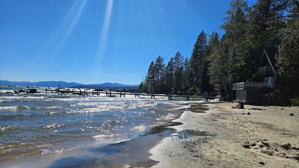 A beach with a wooden walkway, clear skies, and distant mountains.