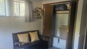 A bedroom with a bed, a bench, a wardrobe, and a window with curtains.