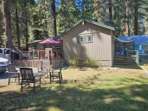A wooden cabin with a fenced deck, surrounded by tall trees.