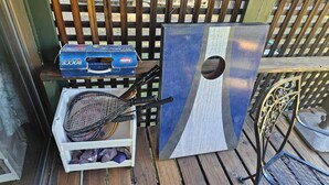 A wooden deck with a grill, a tennis racket, and a storage box.