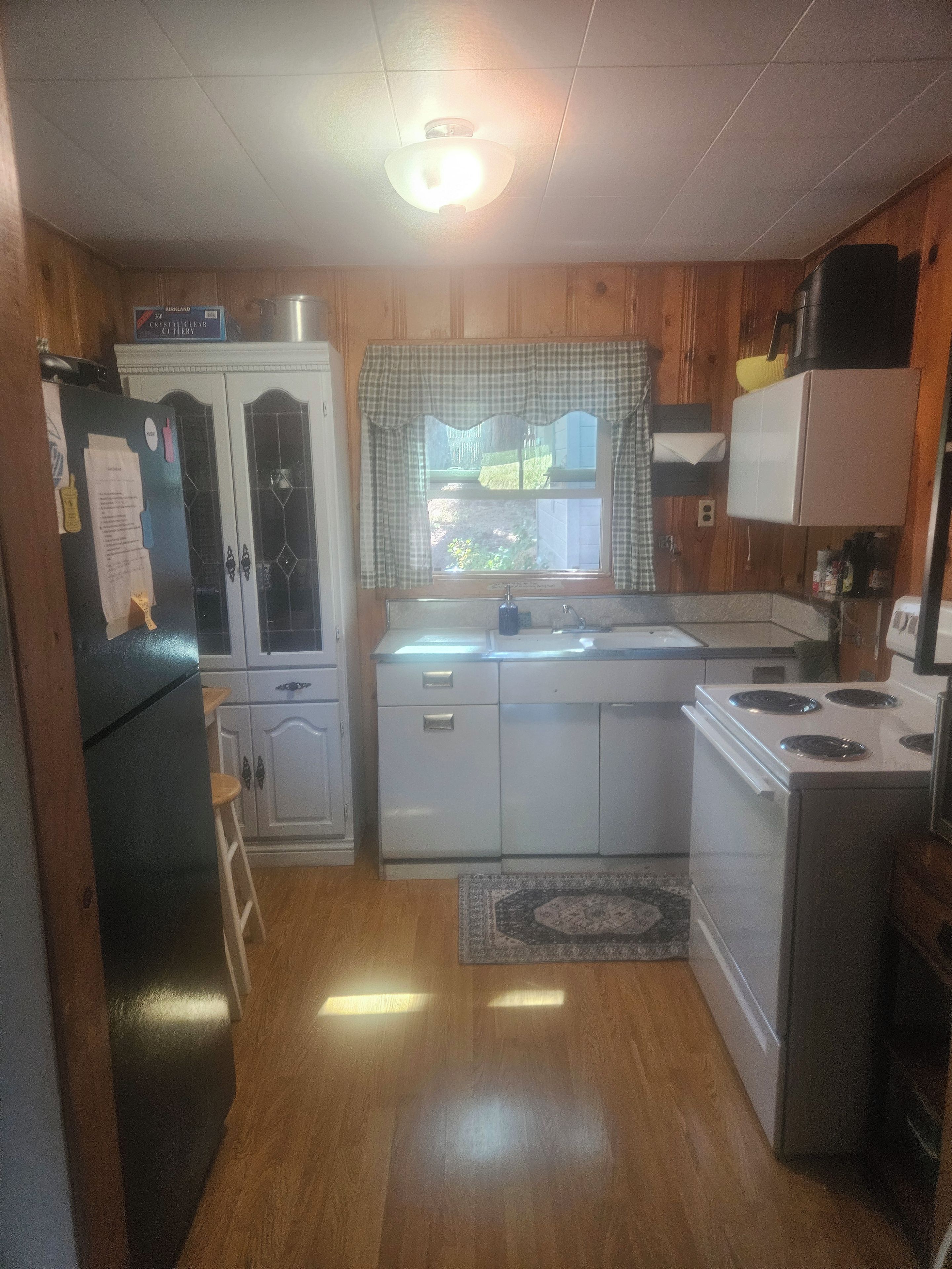 Una cocina compacta con armarios de madera, un refrigerador, una estufa y una ventana con cortina a cuadros.