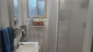 A bathroom with a white sink, a mirror, a towel rack, a window, and a shower enclosure.
