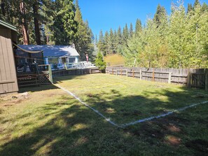 A fenced backyard with a grassy area, a wooden deck, and a building with a sloped roof.