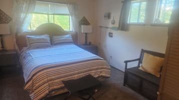 Ein Schlafzimmer mit Bett, Sessel, Nachttisch, Fenster und Lampe.