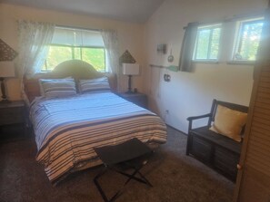 A bedroom with a bed, a chair, a nightstand, a window, and a lamp.