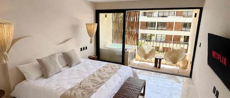 A modern bedroom with a large bed, a ceiling fan, a TV, and a view of a balcony with outdoor furniture.