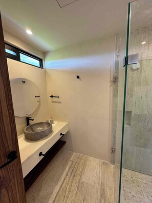 Ein Badezimmer mit einem runden Waschbecken, einem Spiegel und einer Duschkabine aus Glas.