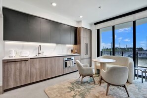 Cozinha moderna com eletrodomésticos embutidos, área de refeições com duas cadeiras e uma janela grande com vista para a cidade.