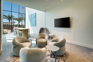A modern lounge area with comfortable seating, a flat-screen TV, and a large window offering a view of palm trees. - 72 Park by Mia Casa (Miami Beach)