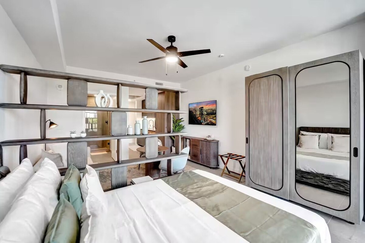A modern bedroom with a bed, a wardrobe, a ceiling fan, and a cityscape painting.