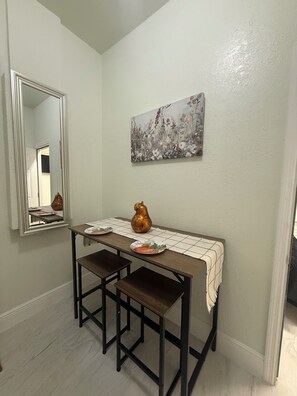 Een eetruimte met een tafel, twee stoelen, een vaas en een schilderij aan de muur.