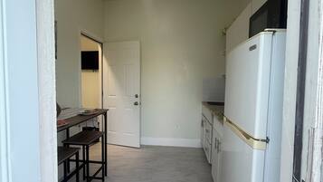 A compact kitchen with a white refrigerator, a dining table with chairs, and a door leading to another room.