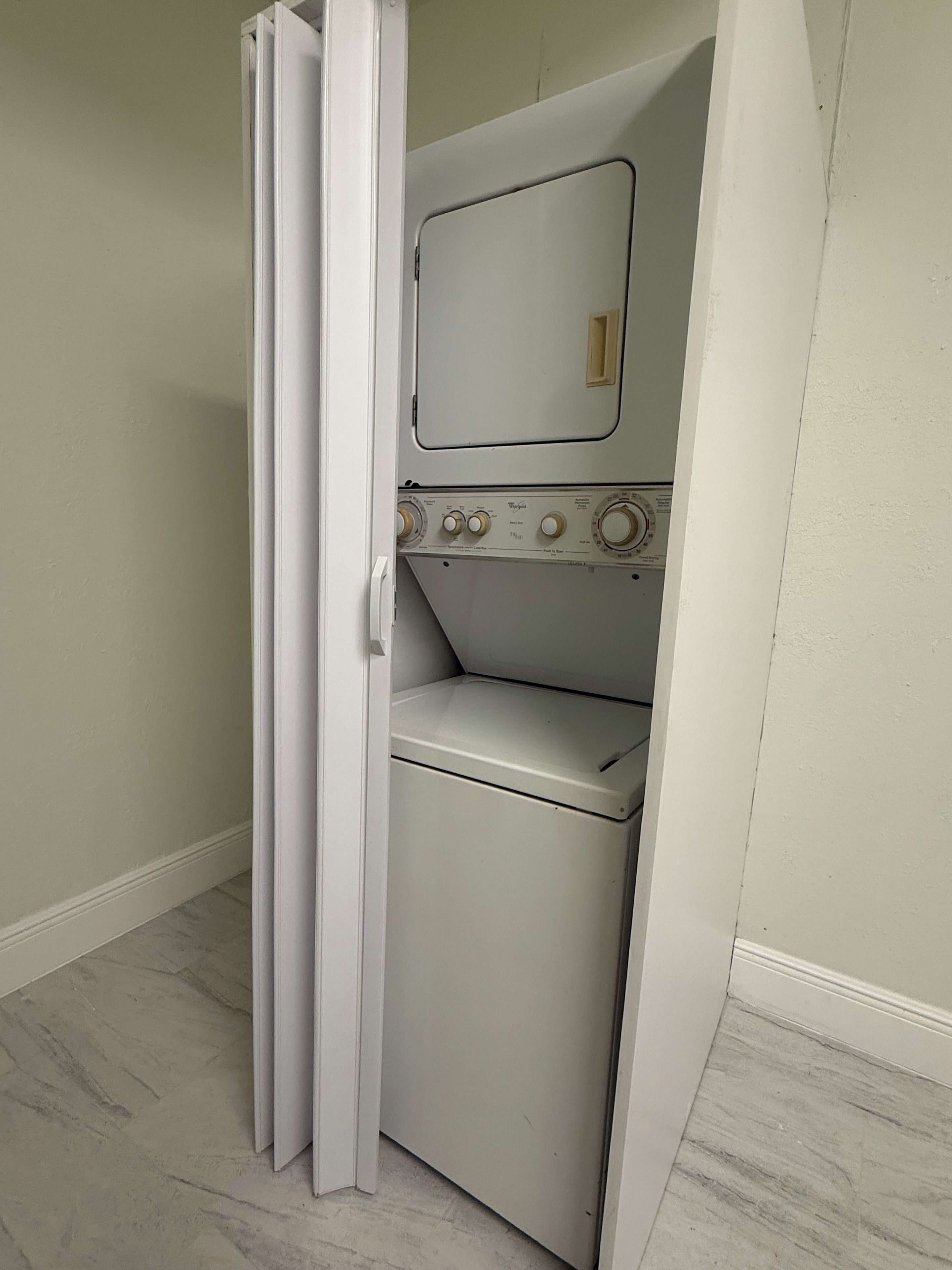 Uma lavanderia compacta com máquina de lavar e secadora, uma porta e um interruptor de luz.