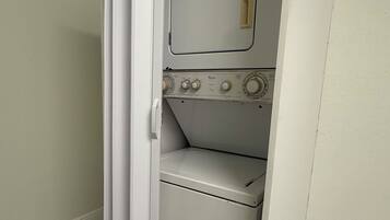 Uma lavanderia compacta com máquina de lavar e secadora, uma porta e um interruptor de luz.