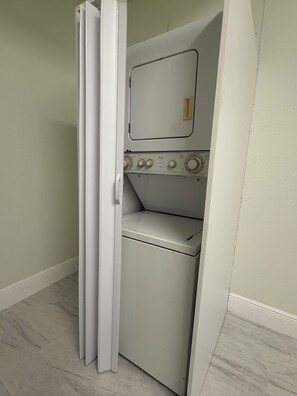 A compact laundry room with a washing machine and dryer, a door, and a light switch. - Private Studio Near RSW, AC, Wi-Fi & Free Parking, Fort Myers/Lehigh Acres (Lehigh Acres)