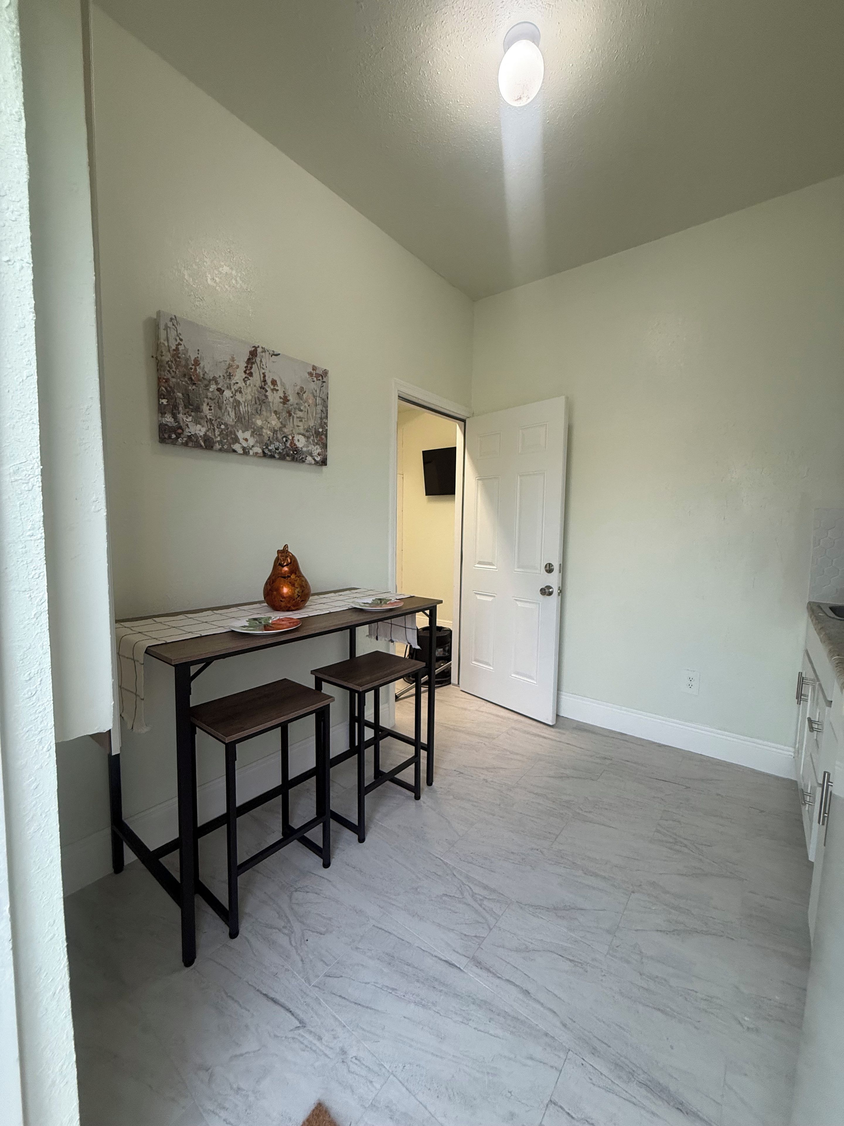 A kitchen with a white countertop, two bar stools, a vase, and a painting on the wall.
