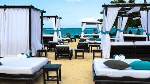 Habitación de hotel frente a la playa con varias camas, cada una con ropa blanca y detalles azules, y vista al océano.