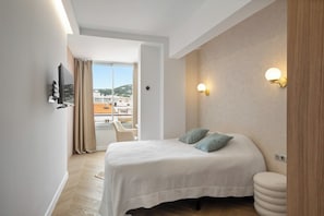 A hotel room with a bed, a TV, a small table, and a view of the city. - Vrbo Property (Cannes)
