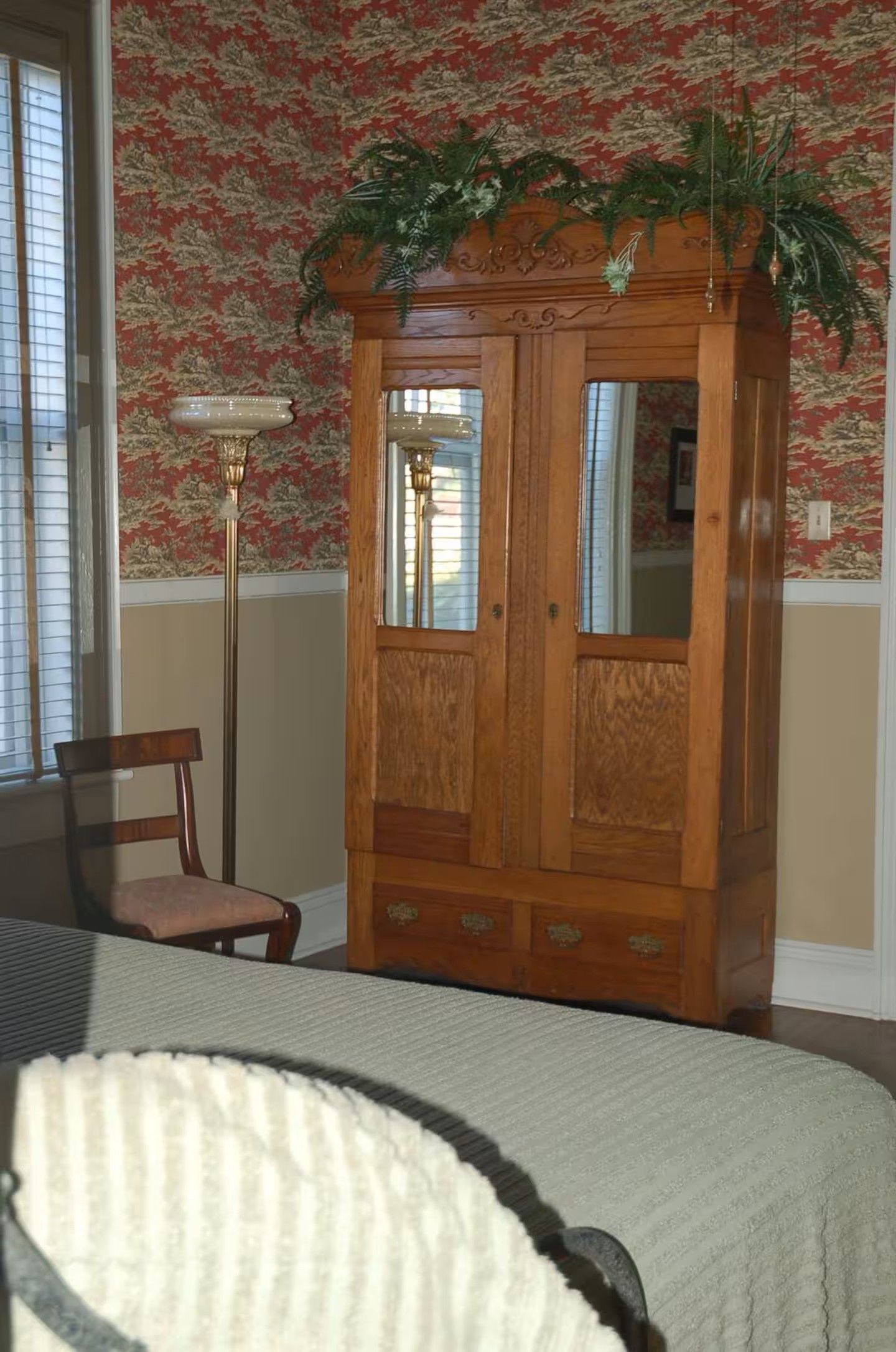 A room with a wooden armoire, a chair, and a bed.