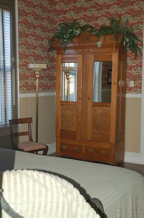 A room with a wooden armoire, a chair, and a bed.