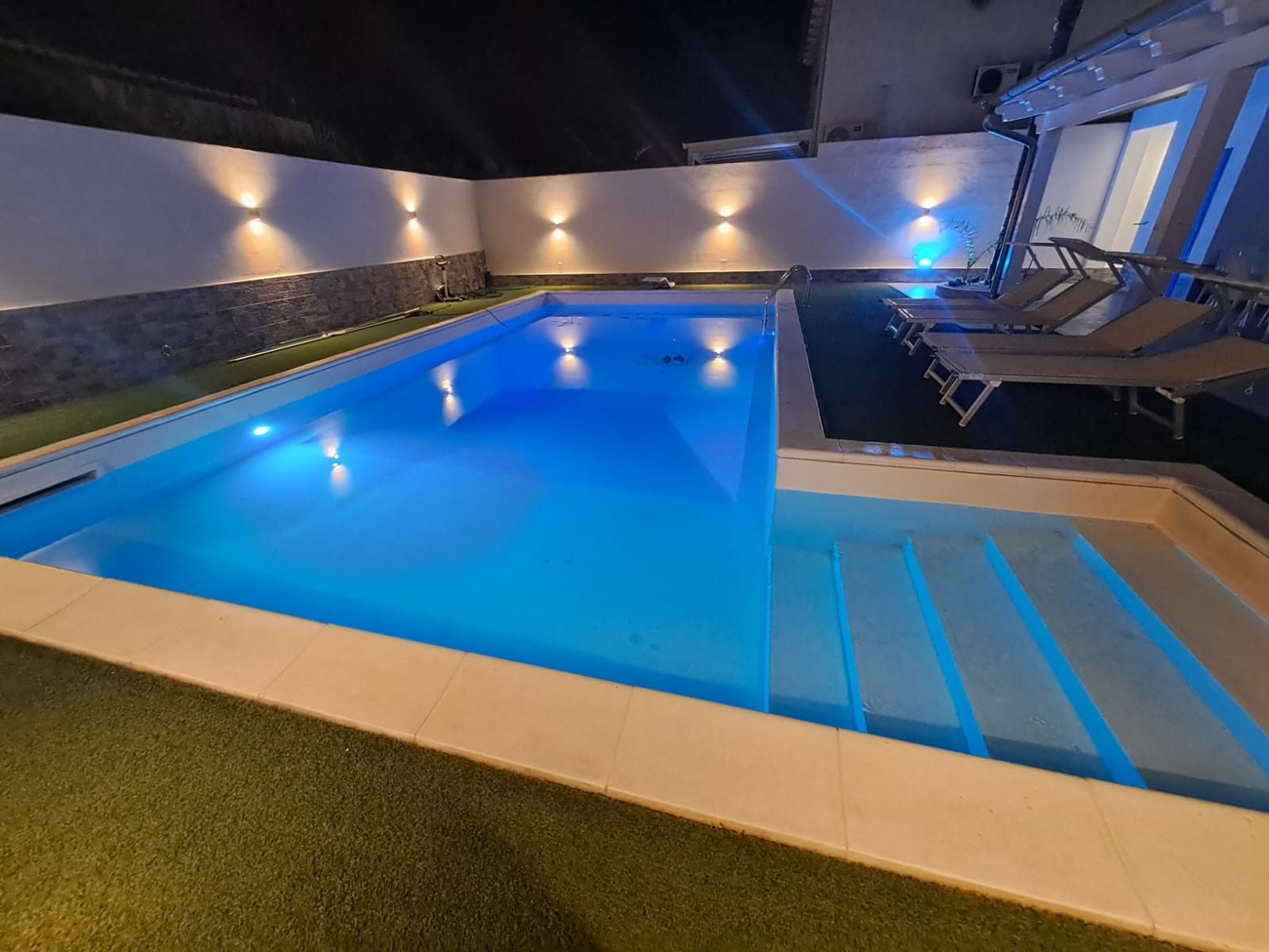 Ein Pool mit Stufen, umgeben von Wänden mit integrierter Beleuchtung.