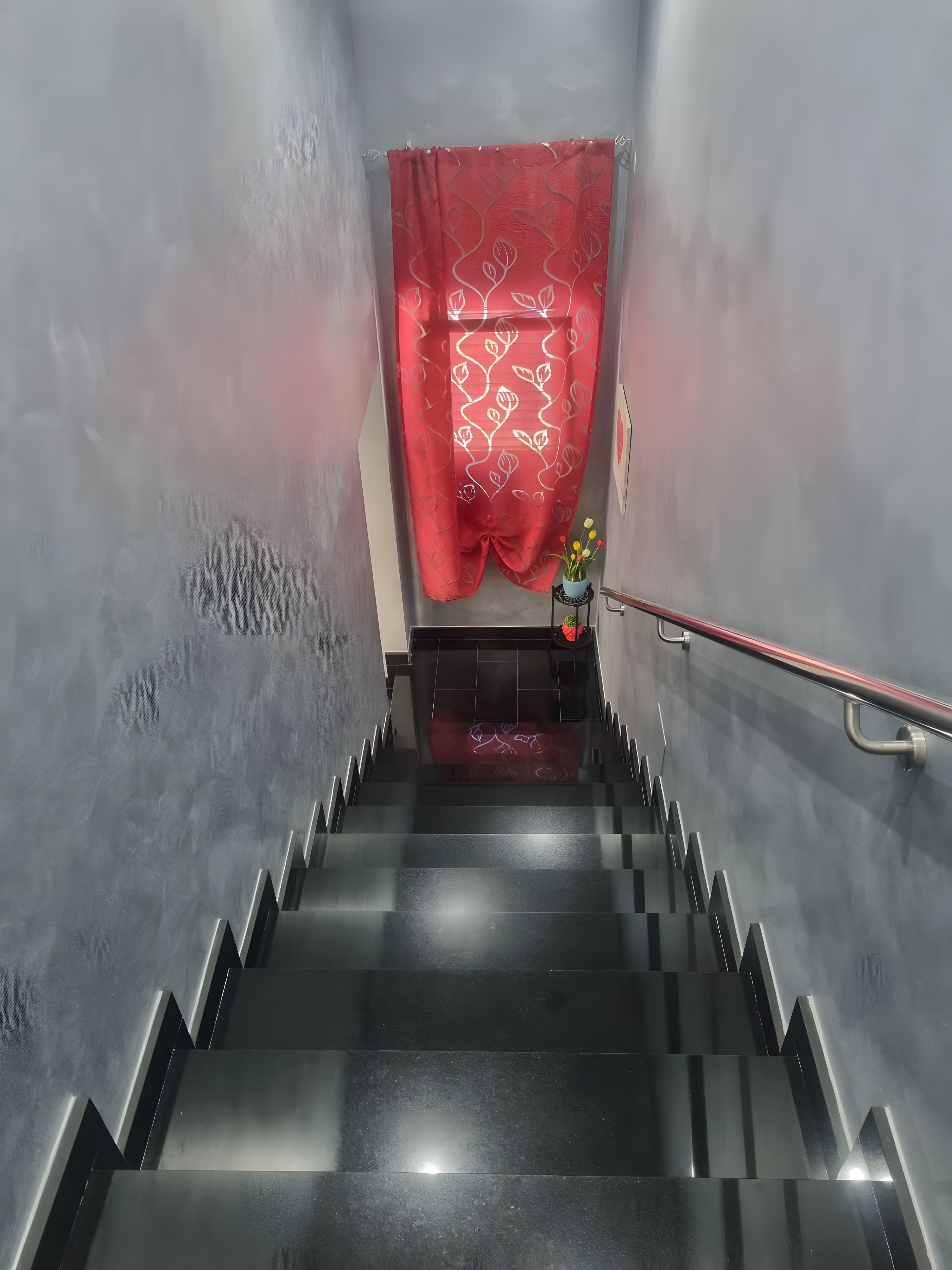 Eine Treppe mit rotem Vorhang oben, Metallgeländern und einem kleinen Tisch mit Blumen.