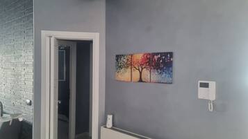 Una habitación con pared gris, una puerta que da a otra estancia, un radiador y un termostato fijado a la pared.