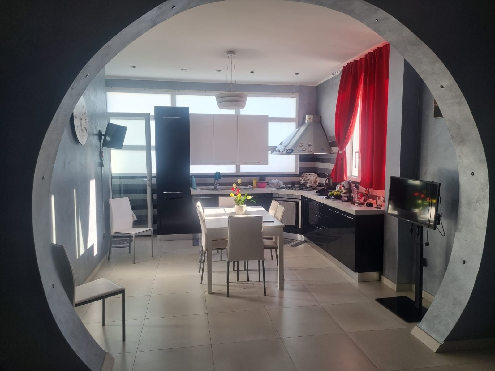 Cozinha moderna com área de refeições, uma janela grande e cortina vermelha.