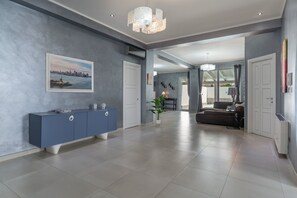 A modern interior with a grey wall, a blue console, a cityscape painting, and a black sofa.