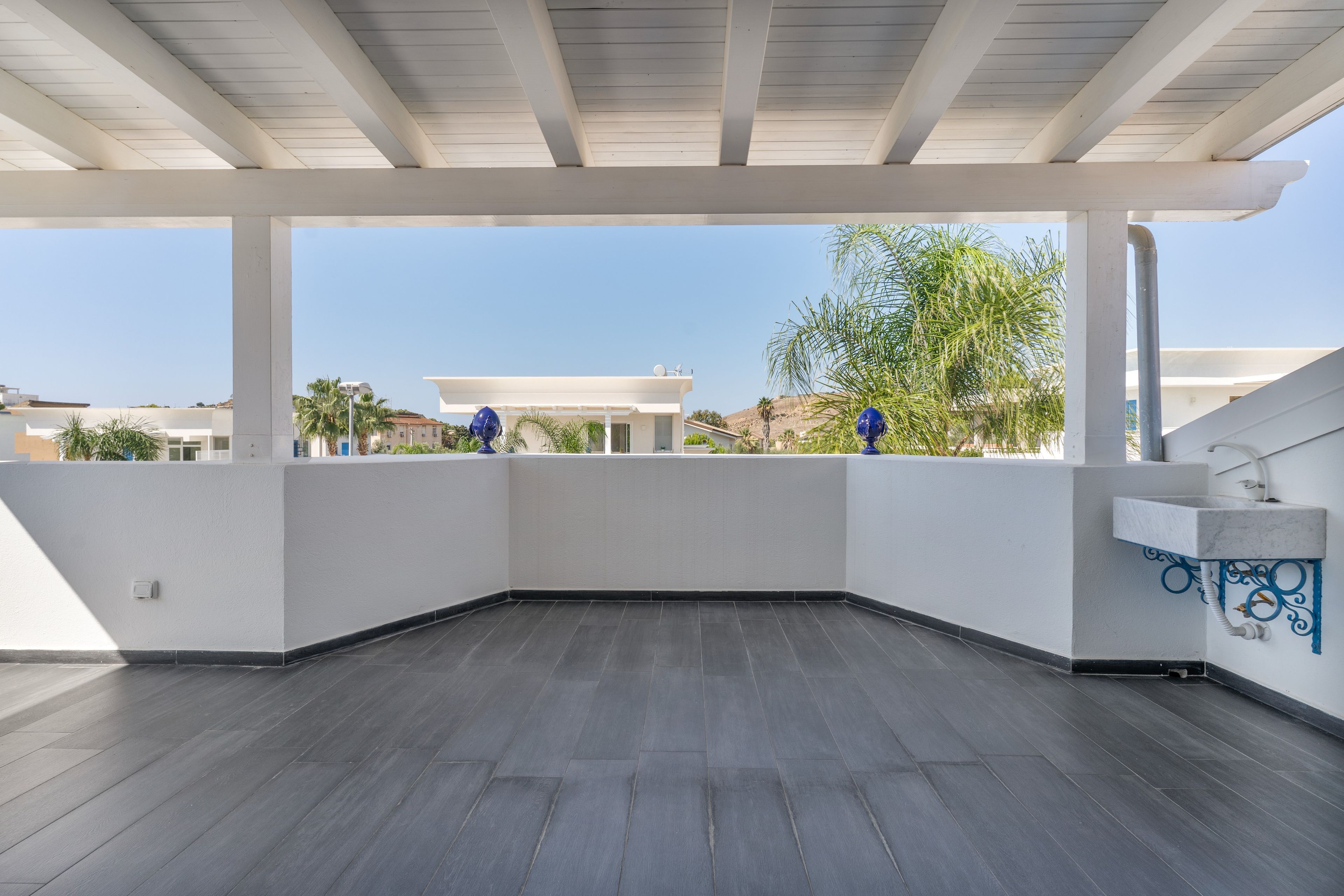 A covered outdoor area with a flat roof, white walls, and a grey floor.