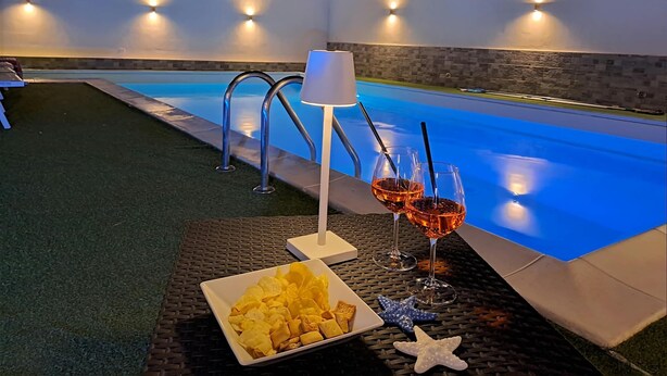 Un espace piscine extérieur avec une table préparée pour deux personnes, comprenant des collations et des boissons.