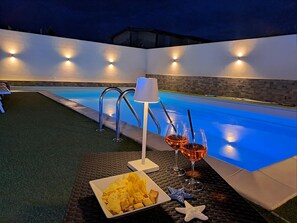 An outdoor pool area with a table set for two, including snacks and drinks.