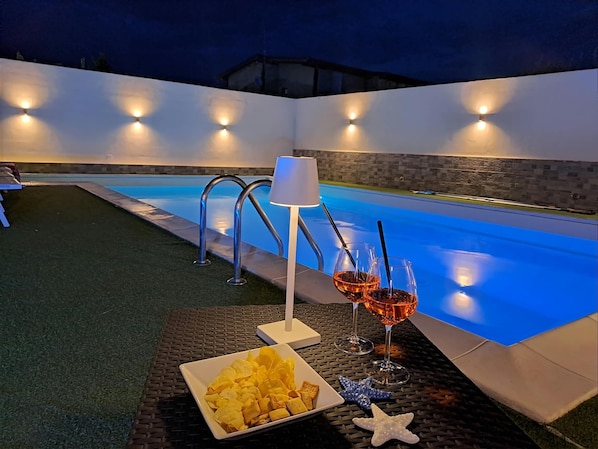 Een buitenzwembad met een tafel voor twee, compleet met snacks en drankjes.