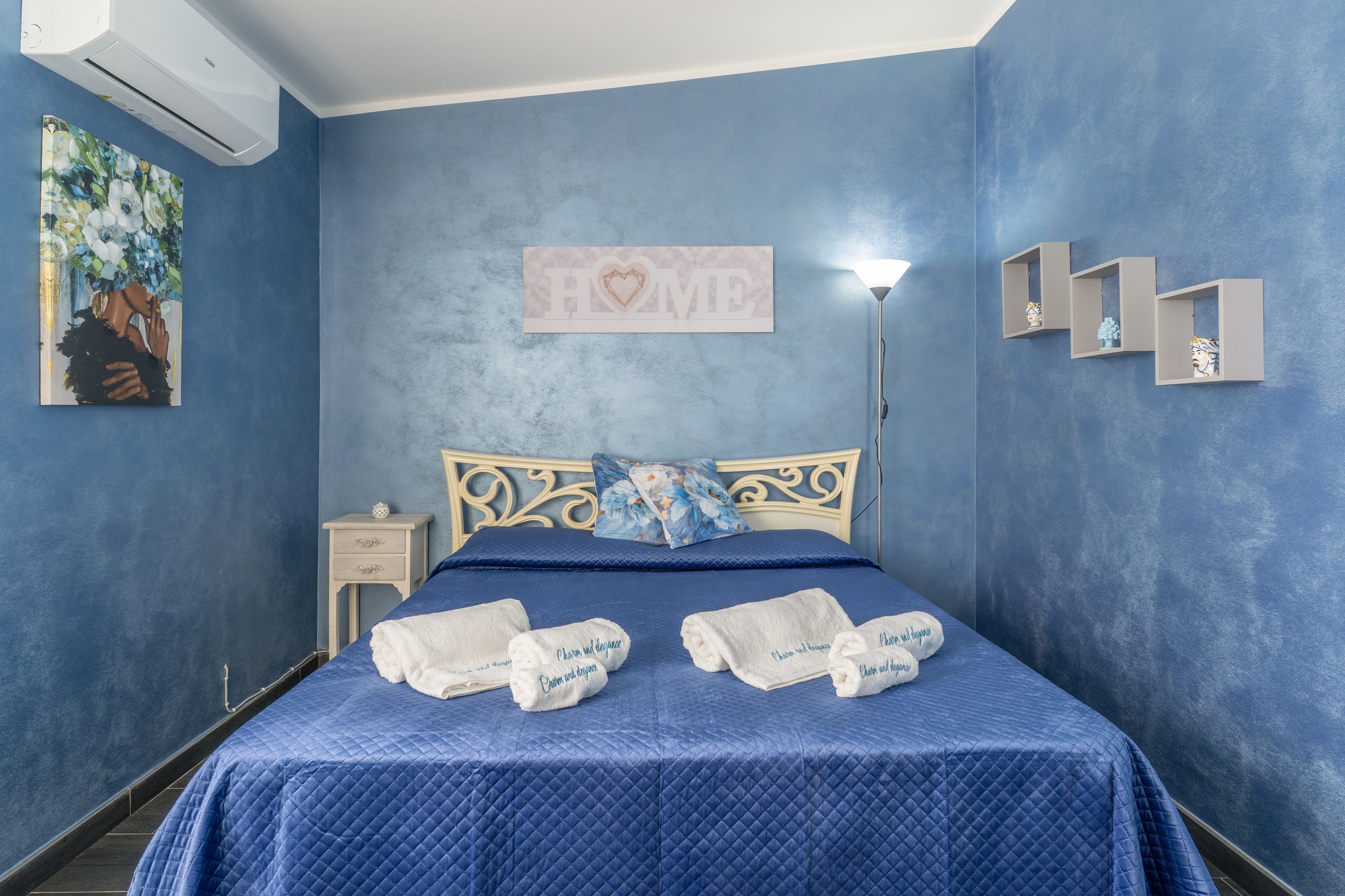 A bedroom with a bed, a nightstand, a wall-mounted shelf, and a painting.